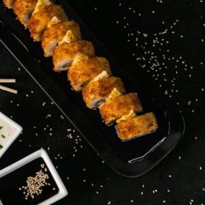 Gourmet crispy sushi rolls on a black plate with dipping sauces, perfect for a sophisticated meal.