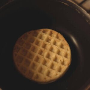 A single waffle being cooked in a frying pan on a stove in a kitchen setting.
