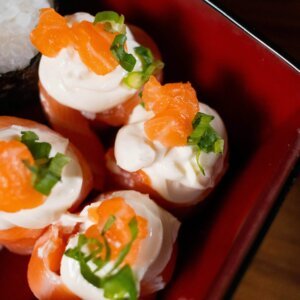 Close-up of sushi rolls topped with salmon, cream cheese, and green onions in a red dish.